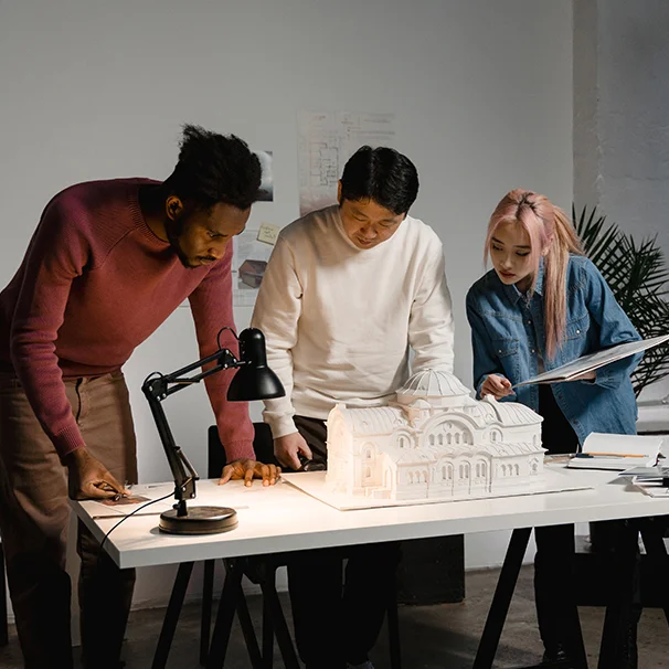 Group of architects reviewing a model building on a table in the office, discussing design and construction details.